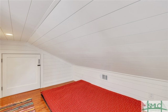 bonus room with vaulted ceiling, wood finished floors, and wood walls