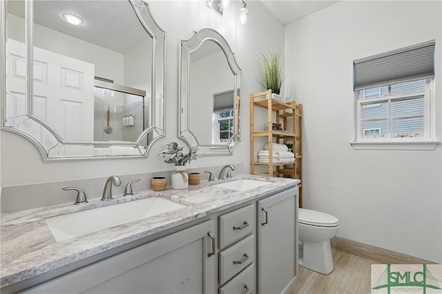 full bath with a shower with shower door, double vanity, toilet, wood finished floors, and baseboards