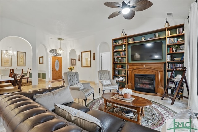 living area featuring arched walkways, a chandelier, a glass covered fireplace, ceiling fan, and lofted ceiling