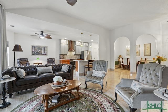 living room with arched walkways, ceiling fan, light wood finished floors, and lofted ceiling