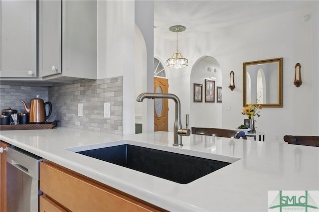 kitchen featuring a sink, decorative backsplash, light countertops, dishwasher, and decorative light fixtures
