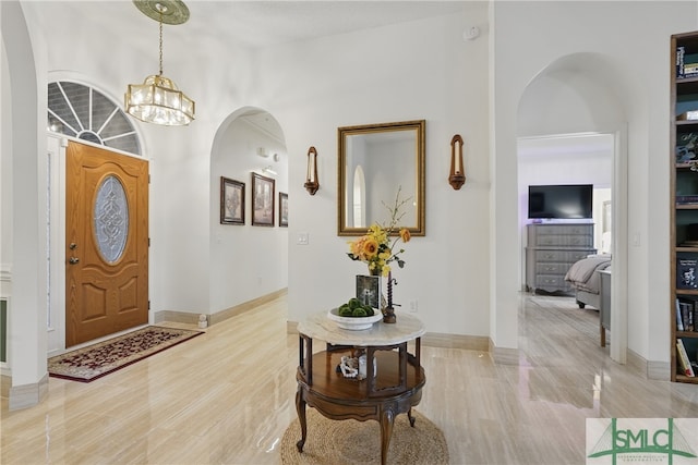 entryway featuring a chandelier, baseboards, arched walkways, and light wood finished floors