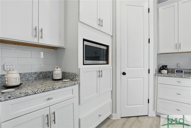 240 Blackjack Oak Dr W, Richmond Hill, GA 31324 - kitchen with tasteful backsplash, stainless steel microwave, light wood-style flooring, white cabinets, and light stone counters