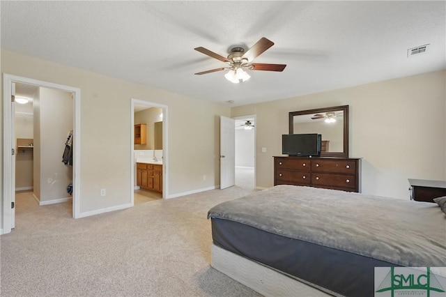 bedroom featuring light colored carpet, baseboards, connected bathroom, a ceiling fan, and a walk in closet
