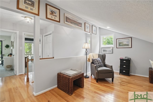 living area featuring light wood-style floors, healthy amount of natural light, a textured ceiling, vaulted ceiling, and an upstairs landing