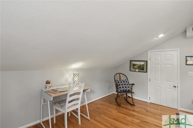 office area featuring vaulted ceiling, light wood-style flooring, a textured ceiling, and baseboards