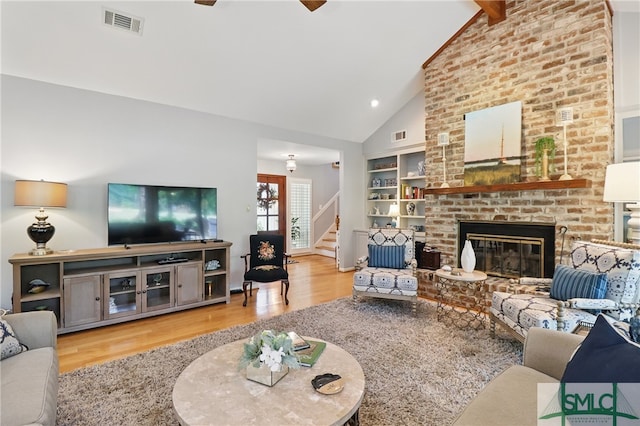 living room with wood finished floors, stairs, a fireplace, built in features, and high vaulted ceiling
