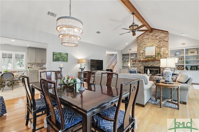 dining area with light wood-style floors, a brick fireplace, stairs, ceiling fan, and a chandelier