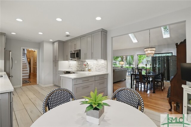 kitchen with gray cabinetry, appliances with stainless steel finishes, backsplash, light wood-style floors, and recessed lighting