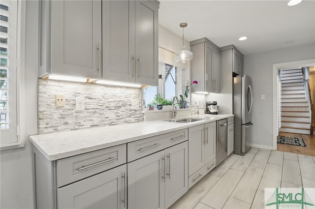 kitchen featuring gray cabinetry, appliances with stainless steel finishes, a sink, decorative backsplash, and pendant lighting