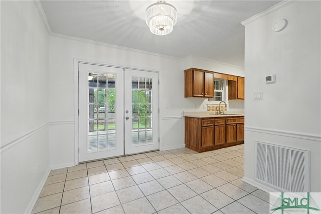 kitchen with a sink, brown cabinetry, light countertops, french doors, and crown molding