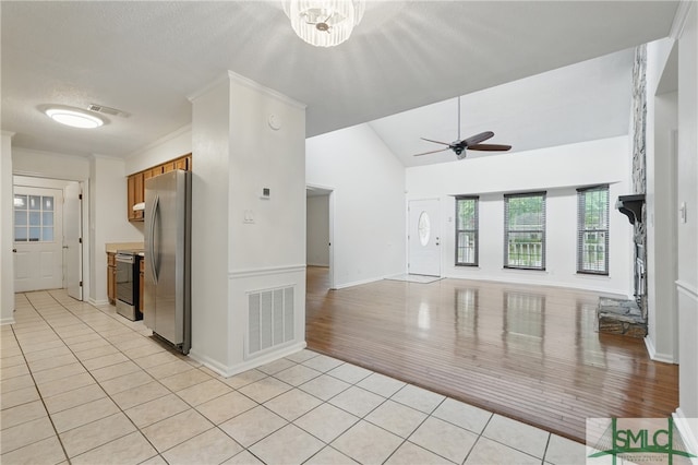 kitchen with appliances with stainless steel finishes, light tile patterned floors, brown cabinets, baseboards, and vaulted ceiling