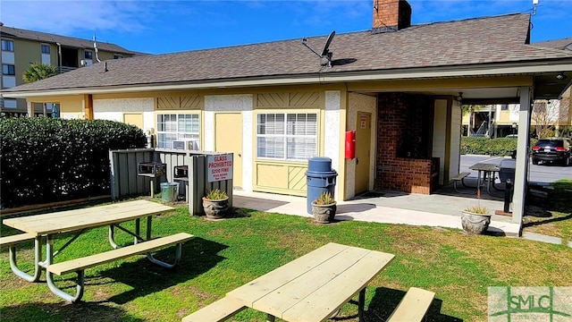 85 Van Horne Ave Unit 12A, Tybee Island, GA 31328 - rear view of house featuring a shingled roof, a yard, a chimney, and brick siding
