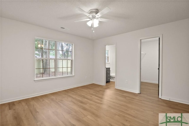 unfurnished bedroom with light wood-type flooring, a spacious closet, a textured ceiling, baseboards, and ensuite bathroom