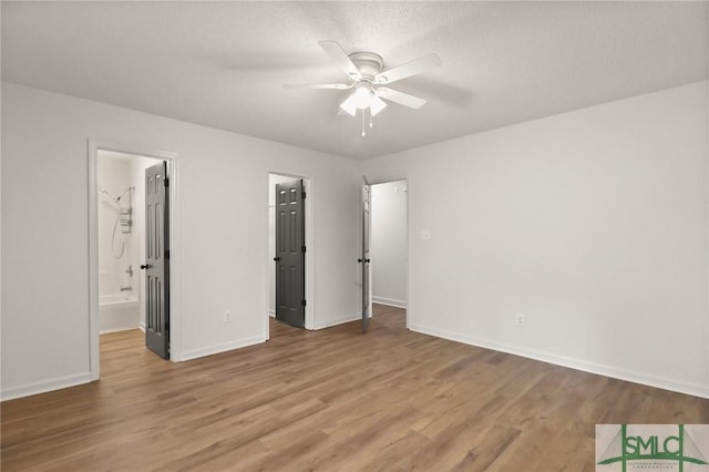unfurnished bedroom with wood finished floors, baseboards, connected bathroom, and ceiling fan