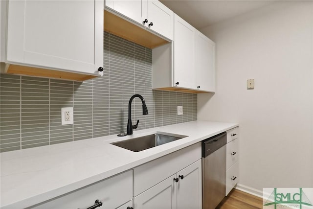 kitchen with stainless steel dishwasher, a sink, backsplash, light countertops, and white cabinets
