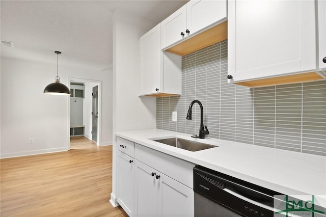 kitchen with stainless steel dishwasher, a sink, tasteful backsplash, light countertops, and white cabinets