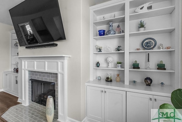 detailed view of built in shelves, wood finished floors, a fireplace with flush hearth, and baseboards