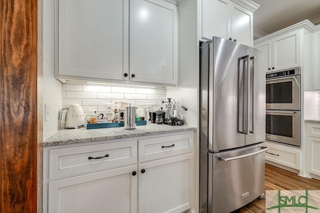 1840 Mccall Rd, Rincon, GA 31326 - kitchen featuring appliances with stainless steel finishes, wood finished floors, white cabinets, decorative backsplash, and light stone counters