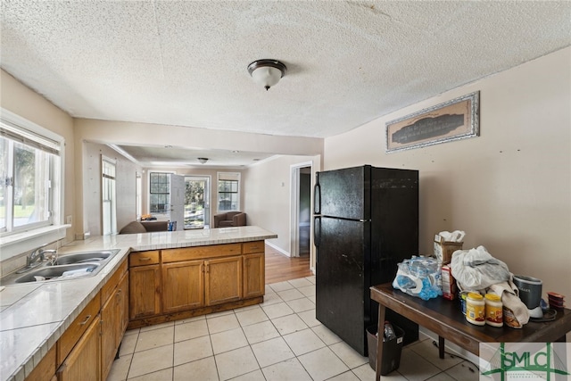3808 Elmdale Ave, Savannah, GA 31405 - kitchen with freestanding refrigerator, brown cabinetry, a peninsula, a sink, and light countertops