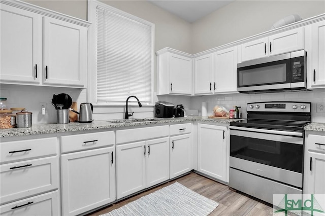 412 E 40th St E, Savannah, GA 31401 - kitchen with appliances with stainless steel finishes, a sink, white cabinetry, light wood-style flooring, and backsplash