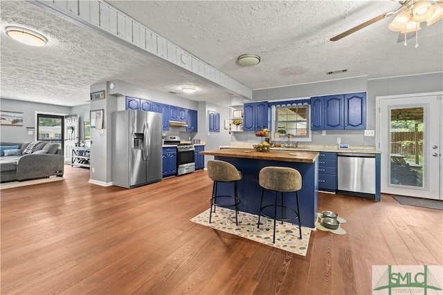 81 Quail Ln, Richmond Hill, GA 31324 - kitchen with blue cabinets, stainless steel appliances, butcher block counters, wood finished floors, and a textured ceiling
