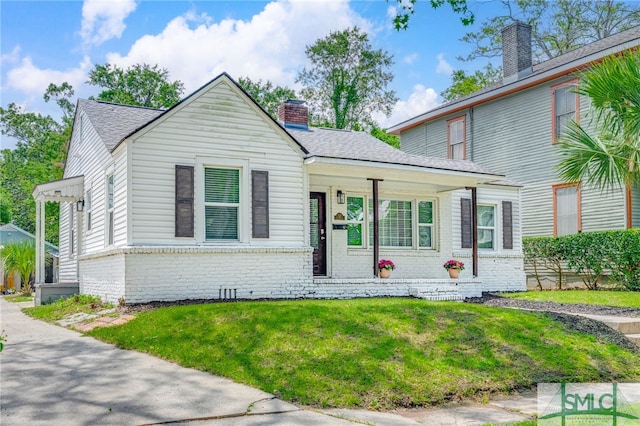 view of front of house with brick siding, a chimney, a front yard, and a shingled roof