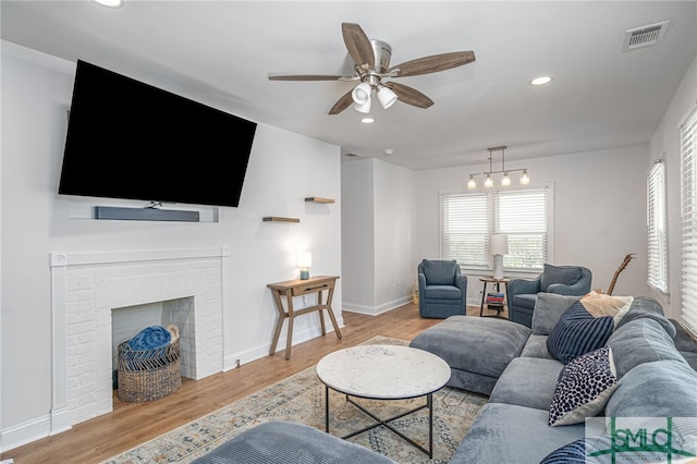 living area with ceiling fan, light wood-type flooring, recessed lighting, baseboards, and a brick fireplace