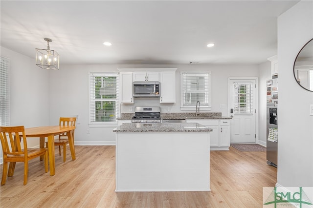 kitchen featuring stainless steel appliances, white cabinetry, a sink, a chandelier, and healthy amount of natural light