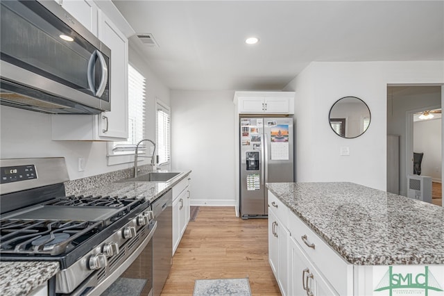kitchen featuring appliances with stainless steel finishes, a sink, white cabinets, light wood-style floors, and light stone countertops