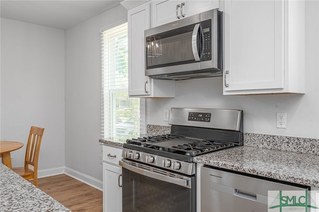 kitchen with appliances with stainless steel finishes, light wood-type flooring, white cabinetry, and light stone counters