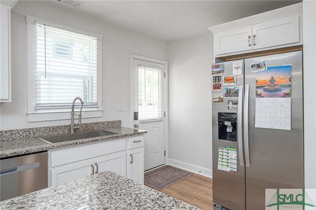 kitchen with stainless steel appliances, a sink, light wood-style floors, and white cabinetry
