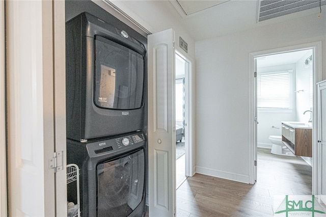 washroom featuring stacked washing machine and dryer, light wood-style floors, and baseboards