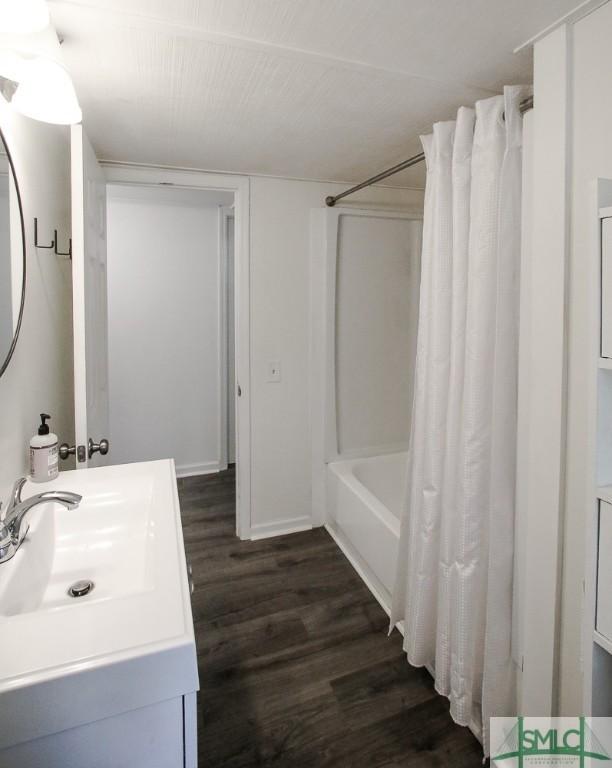 full bath with wood finished floors, shower / bathtub combination with curtain, and vanity