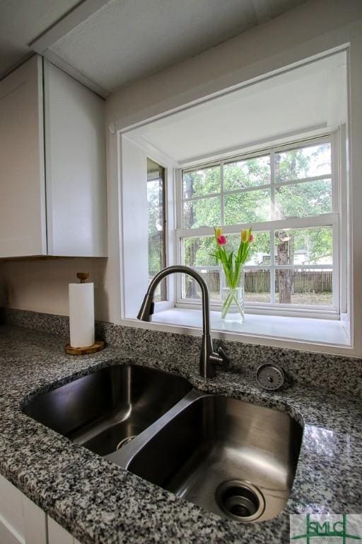 kitchen view of a sink, white cabinets, and dark stone countertops