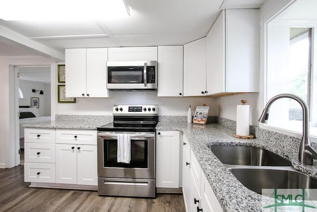 kitchen with stainless steel appliances, a sink, wood finished floors, white cabinetry, and light stone countertops