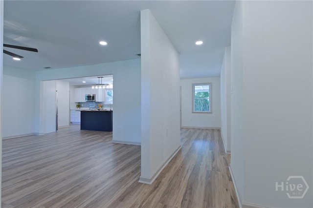hallway featuring light wood finished floors, baseboards, and recessed lighting