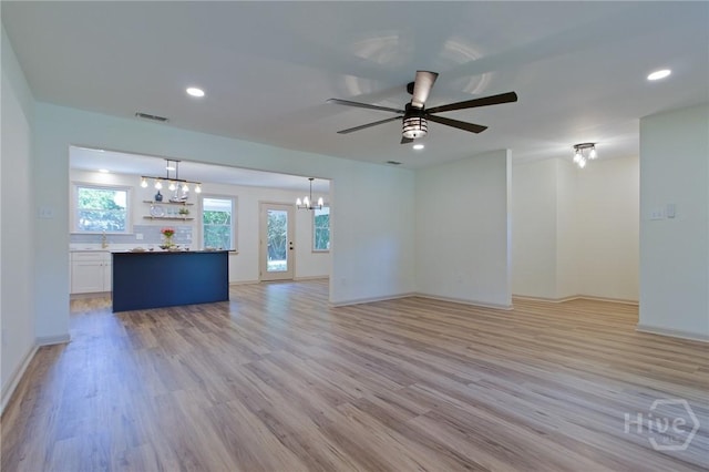 unfurnished living room featuring a chandelier, light wood-style flooring, a ceiling fan, a sink, and recessed lighting