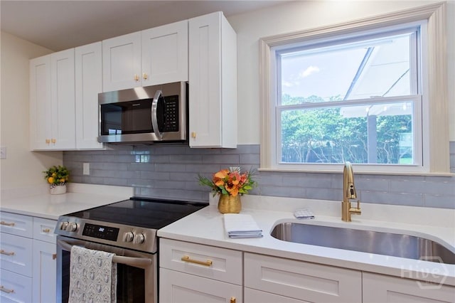 kitchen featuring stainless steel appliances, a sink, backsplash, and white cabinets