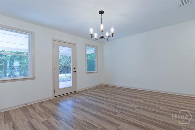 unfurnished dining area featuring a chandelier, plenty of natural light, wood finished floors, and baseboards