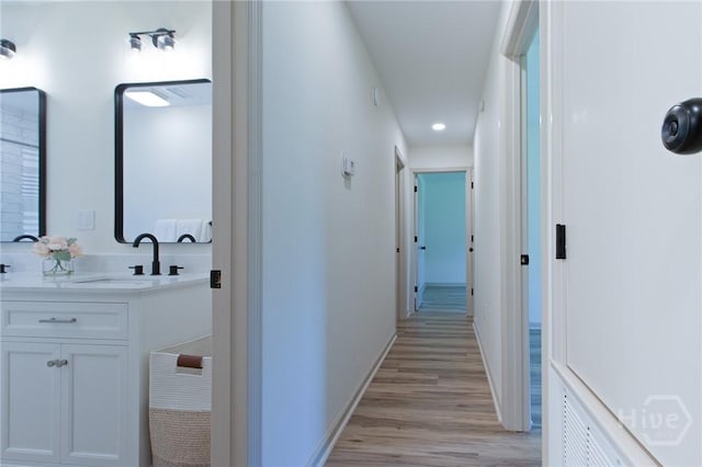 hallway with a sink, light wood-style flooring, recessed lighting, and baseboards