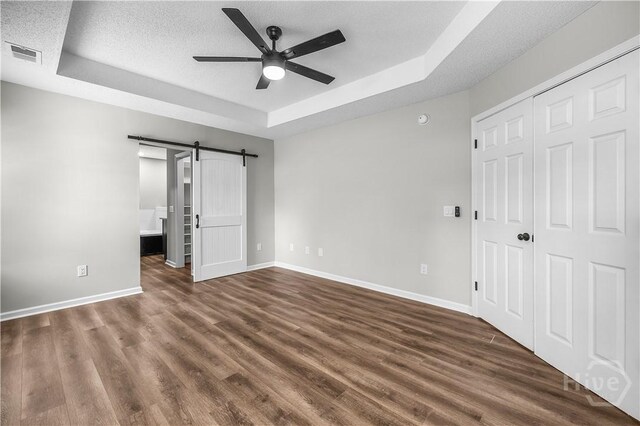 407 Middleton St, Pooler, GA 31322 - unfurnished bedroom featuring a tray ceiling, baseboards, a barn door, dark wood finished floors, and a textured ceiling
