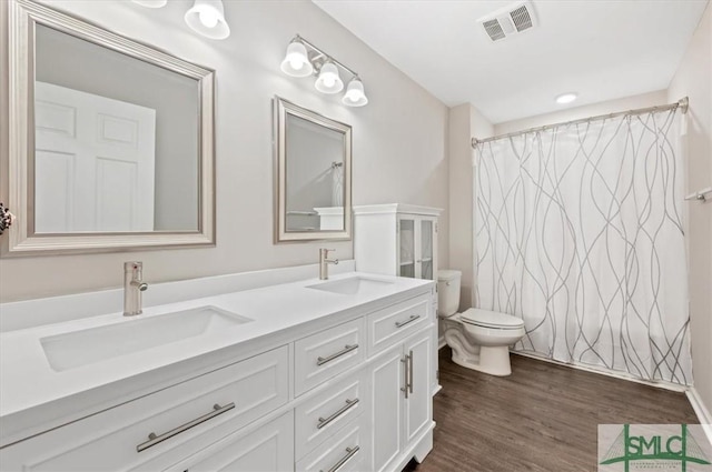 full bath featuring toilet, wood finished floors, double vanity, and curtained shower