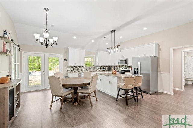 dining space with lofted ceiling, a chandelier, light wood-style flooring, recessed lighting, and french doors