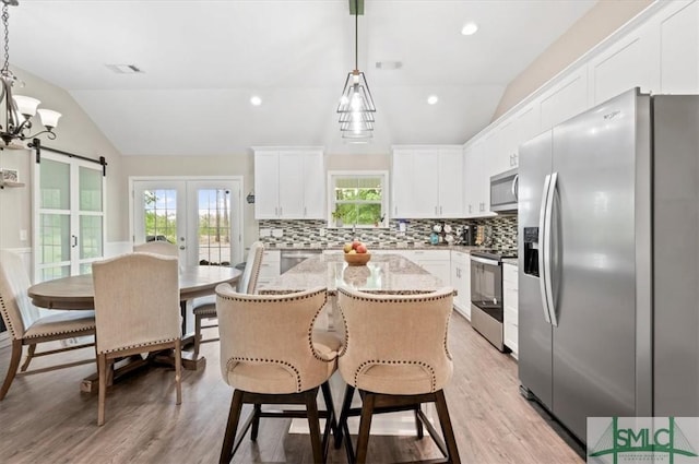 kitchen with appliances with stainless steel finishes, vaulted ceiling, tasteful backsplash, a barn door, and light wood-type flooring