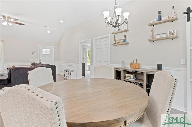 dining area featuring vaulted ceiling, a ceiling fan, a barn door, a chandelier, and wainscoting