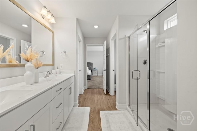 full bath featuring a shower stall, double vanity, wood finished floors, baseboards, and recessed lighting