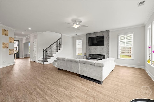 living area featuring ornamental molding, stairs, a large fireplace, ceiling fan, and baseboards