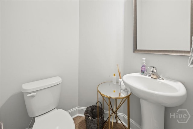 half bath featuring wood finished floors, toilet, and baseboards