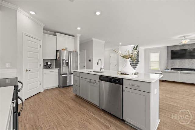 kitchen with appliances with stainless steel finishes, a sink, crown molding, open floor plan, and an island with sink